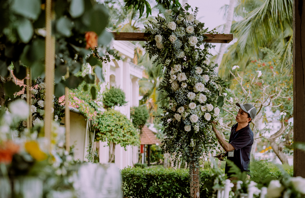 Florist arranging a white and green floral installation for an outdoor wedding ceremony in Danang