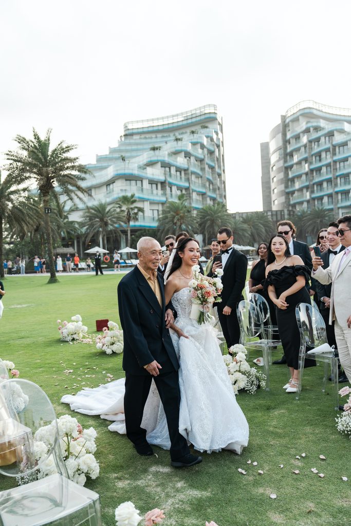 Bride walking down the flower-lined aisle with her father at a beachfront wedding ceremony at Vinpearl Nam Hoi An