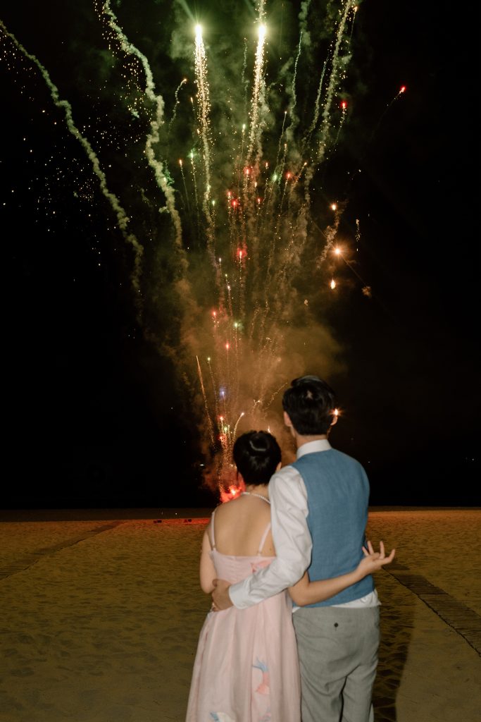 Couple watching a spectacular fireworks display on the beach at Fusion Resort & Villas Da Nang at night.