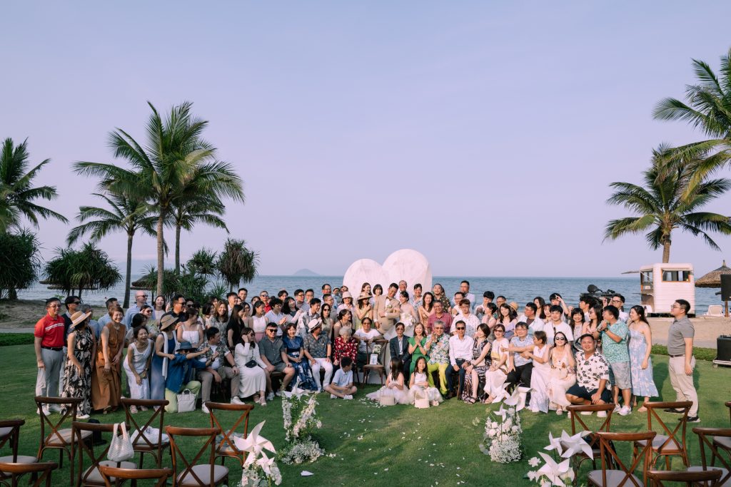 Large group of wedding guests gathered on a beachfront lawn after an outdoor ceremony
