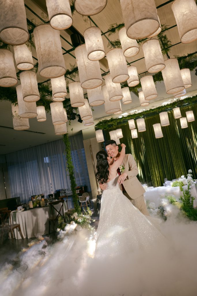 Bride and groom kissing under hanging paper lantern installations with greenery backdrop at an indoor wedding reception