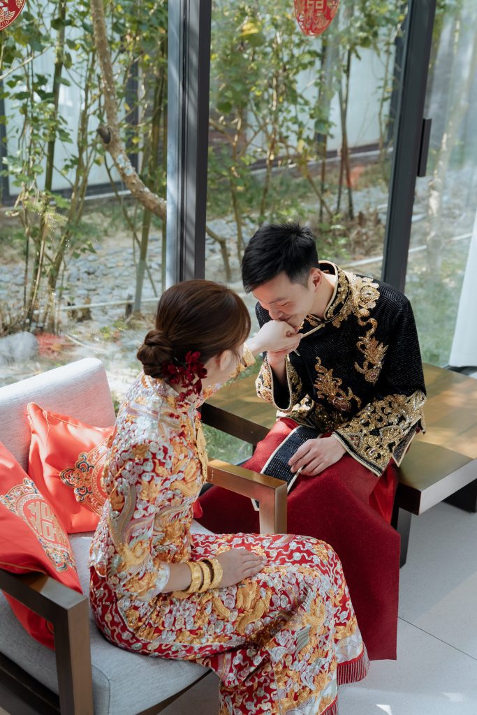 A Hong Kong bride and groom share a traditional wedding moment in ornate red-and-gold attire, celebrating their cultural heritage during their destination wedding in Da Nang.