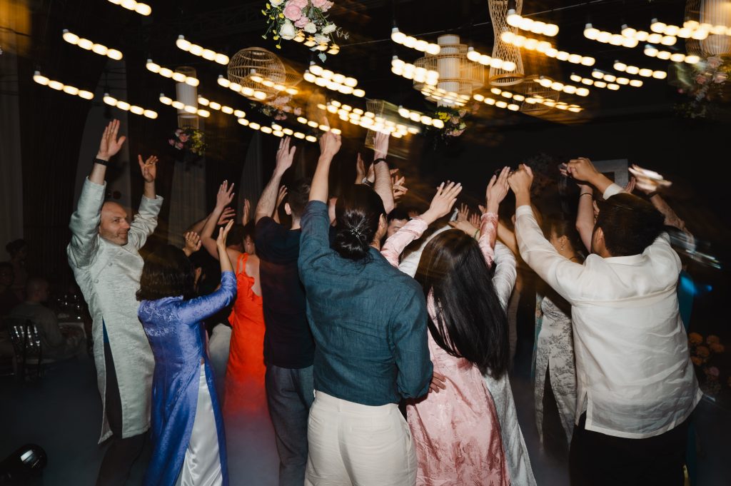Wedding guests dancing with hands raised under string lights and rattan pendant lanterns during an evening after-party at Naman Retreat Danang.