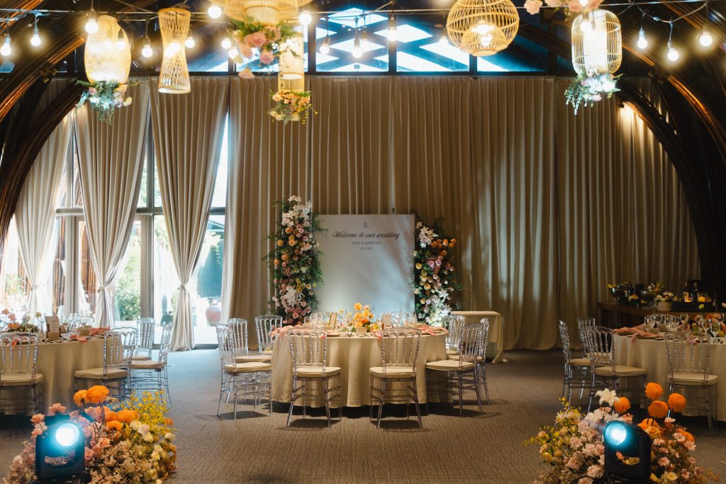 Naman Hall reception at Naman Retreat Danang, showing arched bamboo ceiling, rattan pendant lights, and a round table setting with a floral welcome sign reading "Welcome to our wedding."